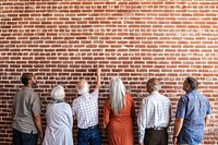 Senior people standing together point at a brick wall mockup 