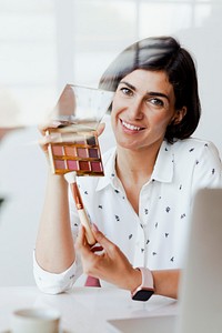 Happy women displaying an eye shadow palette with a laptop