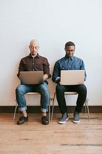 Men using their laptops by a white wall