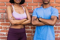 Sporty couple standing with arms crossed by a brick wall