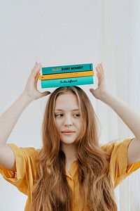 Cheerful blond girl balancing books on her head