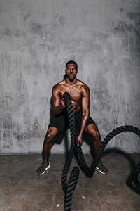 Muscular man doing a battle rope in a gym