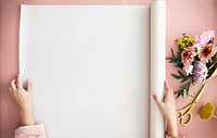 Woman unroll a paper on a pink table by a bouquet of flowers