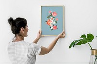 Woman putting up a floral art frame mockup on a wall