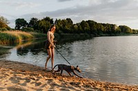 Cheerful woman walks with her Weimaraner dog by the lake
