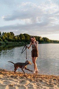 Cheerful woman walks with her Weimaraner dog by the lake