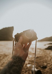 Tattooed man holding a compact camera at the beach