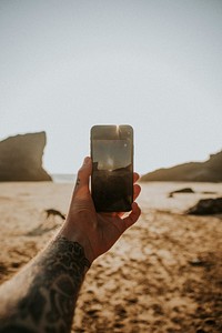 Tattooed man using a mobile phone camera on the beach