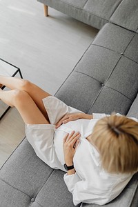 Pregnant blond-haired woman relaxing on a gray sofa