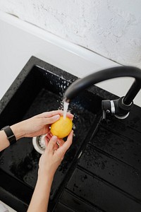 Woman rinsing a yellow lemon in the sink