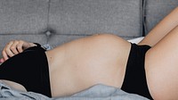 Pregnant woman in a black underwear lying on a gray sofa