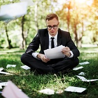 Businessman reading documents sitting on the grass