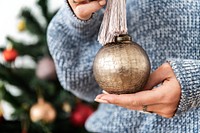 Woman holding a gold bauble in front of a Christmas tree