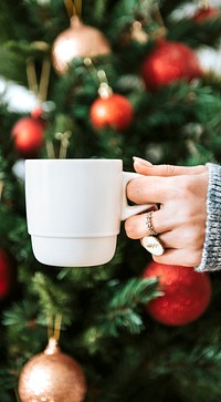 Woman holding a white cup by Christmas tree mobile phone wallpaper