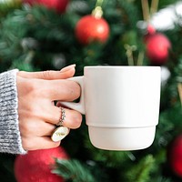 Woman holding a white cup by Christmas tree mockup