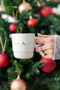 Woman holding a white cup by Christmas tree mockup