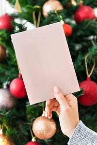 Woman holding a pink Christmas card in front of a Christmas tree