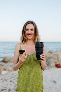 Cheerful woman holding digital camera lenses at the beach