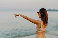 Girl in a beige bikini pointing out to the sea