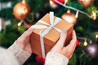 Woman holding a brown present near a Christmas tree