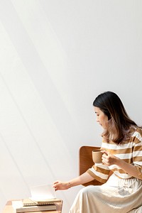 Asian woman drinking coffee while reading a book at home