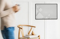 Woman walking past a black photo frame on a white wall mockup