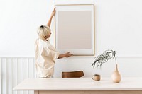 Woman hanging a photo frame on a white wall mockup