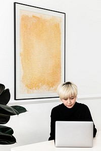 Woman working on her laptop with a frame hanging on a wall mockup