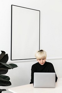 Woman working on her laptop with a blank frame hanging on a wall