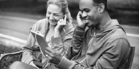 Couple cheerfully listening to music sitting on a park bench
