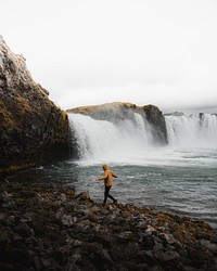 Man by the waterfall walking on rocks 