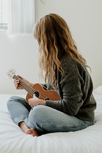 Girl playing ukulele on her bed during quarantine 