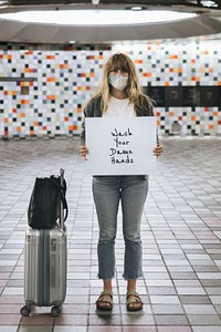 Woman with a suitcase holding wash your damn hands sign during the coronavirus outbreak 