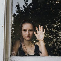 Sad girl staring out the window during a lockdown. 