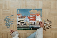 Woman assembling a jigsaw puzzle of Nyhavn, Copenhagen during coronavirus quarantine.