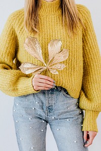 Woman in a yellow knitted sweater holding a golden crisp leaf 