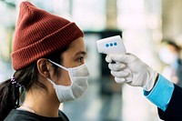 Woman in a medical mask getting her temperature measured by an electronic thermometer 