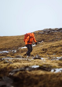 Woman in an orange windbreaker hiking under the rain at the Faroe Islands