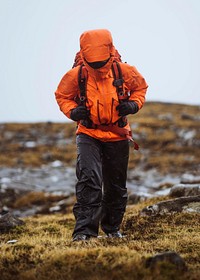 Woman in an orange windbreaker hiking under the rain at the Faroe Islands