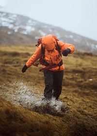 Woman in an orange windbreaker hiking under the rain at the Faroe Islands