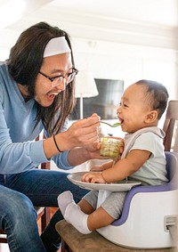 Asian father feeding his son with baby food on a highchair