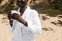 African American senior man in a bathrobe drinking coffee at the beach