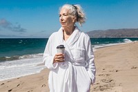 Senior woman in a bathrobe enjoy morning coffee at the beach