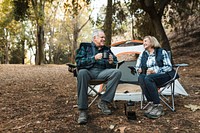 Happy retired couple having coffee by the tent in the forest 