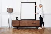 Senior woman adjusting a blank photo frame on a wooden cabinet in a Japandi living room