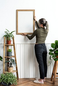 Young woman hanging a frame on the wall 