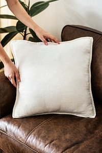 Hand placing a white cushion on a leather couch
