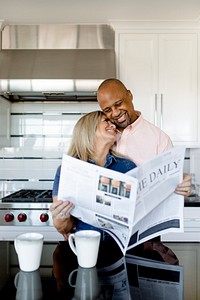Happy couple reading the newspaper together in the kitchen
