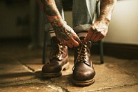 Tattooed man tying boot shoelaces on the floor