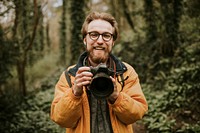 Photographer man smiling while holding camera in the woods